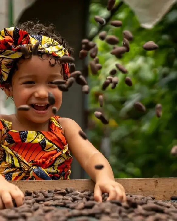 A laughing child tossing cacao beans over a drying bed